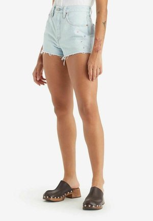 Shorts in denim con orlo sfrangiato, di colore azzurro chiaro, con dettagli ricamati. Abbinati a zoccoli marrone scuro con borchie argentate e base in legno.