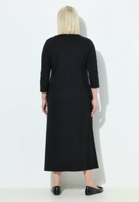 Svart långärmad klänning i en enfärgad design, med rak passform och en något lös känsla, i kombination med svarta platta skor.