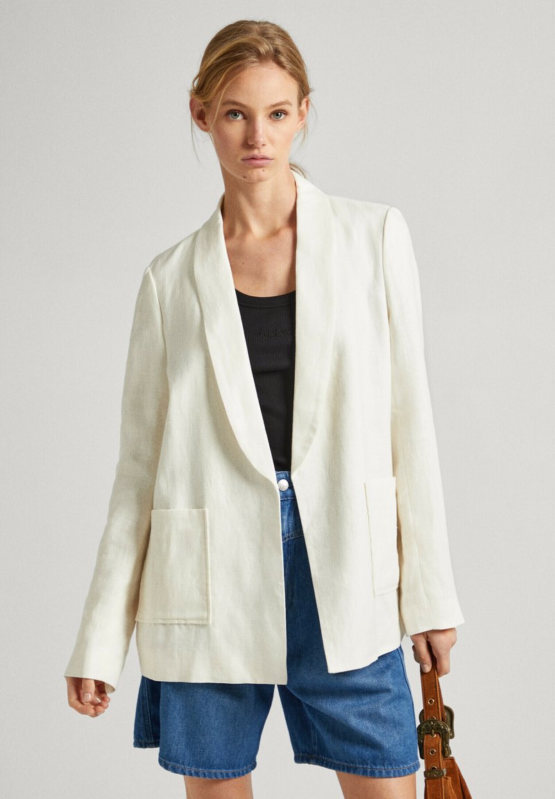 Blazer bianco in lino con apertura frontale, dotato di due tasche anteriori e maniche lunghe, abbinato a pantaloni corti in denim blu.