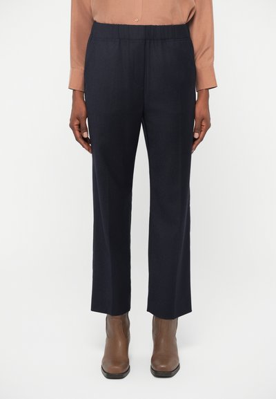 Pantalons navy avec une taille élastique, design à jambe droite et texture lisse. Associés à des bottines marron.