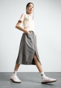 T-shirt bege claro com mangas listradas em rosa, combinado com uma saia de ganga cinza com fenda lateral e cintura elástica. Sapatos brancos com detalhes em rosa.