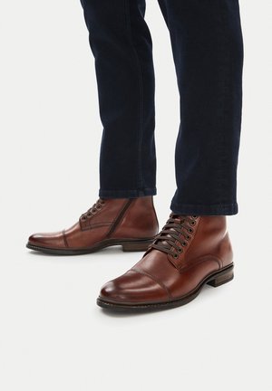 Smeđe kožne gležnjače s vezicama, okruglim vrhom i kontrastnim šavovima, uparene s tamnim trapericama.