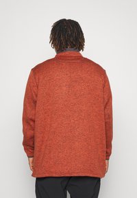 Giacca rossa in fleece con finitura testurizzata, colletto alto e maniche lunghe. Presenta dettagli di cucitura e una silhouette rilassata.