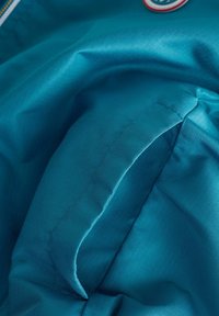 Primo piano di un tessuto blu con una cucitura impunturata e un bordo piegato, che mostra la trama e le linee di cucitura dettagliate.