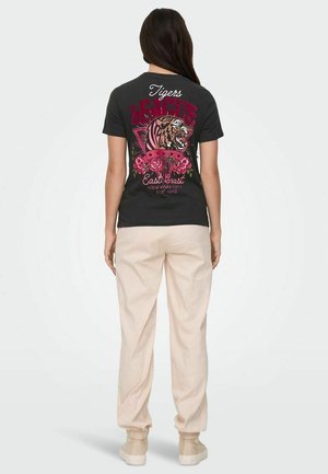 Sort t-shirt med et tiger grafik, prydet med pink og hvide roser, tekst "Tigers East Coast," suppleret af beige, løstsiddende bukser og sneakers.