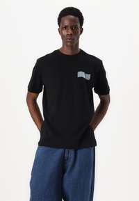 Zwarte katoenen t-shirt met korte mouwen en een gebogen grafische print in lichtblauw op de borst, gecombineerd met losse blauwe denim jeans.