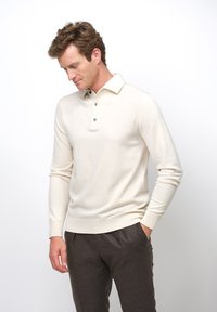 Crème-kleurige lichte gebreide pullover met een geribde kraag en manchetten, voorzien van drie blauwe knopen bij de halslijn.