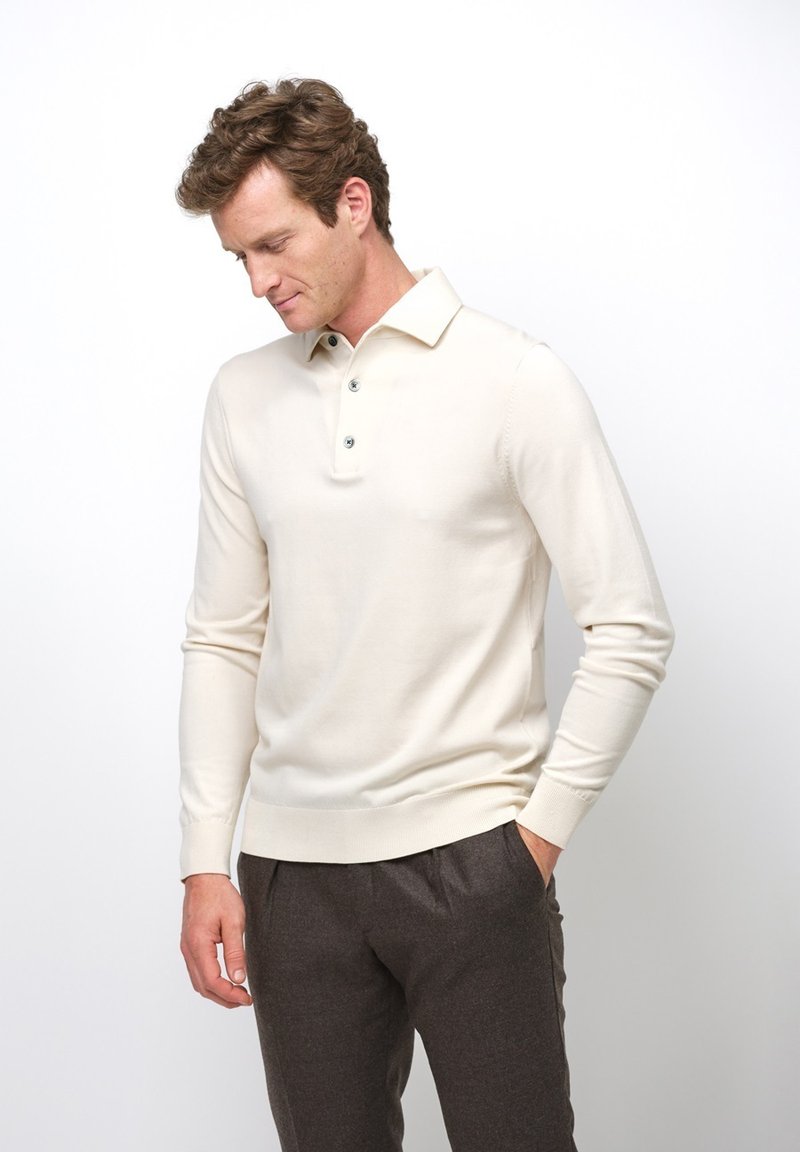 Crème-kleurige lichte gebreide pullover met een geribde kraag en manchetten, voorzien van drie blauwe knopen bij de halslijn.