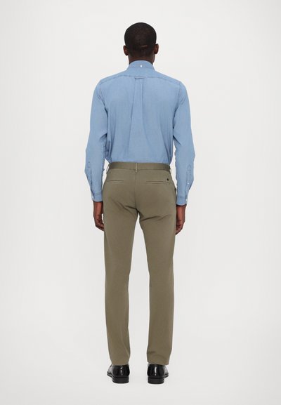 Chemise boutonnée bleu clair à manches longues et pantalon sur mesure vert olive, vue de dos. Des chaussures noires complètent la tenue.