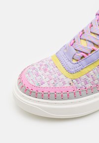 Multikleurige sneaker met een geweven roze en lavendelkleurige bovenkant, gele accenten, grijze zool en contrasterende stiksels. Bevat een ingewikkeld vetersysteem.