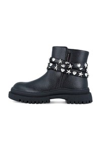 Botas negras hasta el tobillo hechas de cuero texturizado, con tachuelas plateadas de estrellas y corazones en una doble correa y suela gruesa de goma negra.