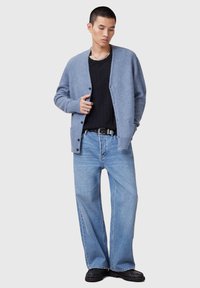 Cardigan azzurro chiaro in materiale morbido, con scollatura a V, chiusura con bottoni e polsini a costine, abbinato a jeans azzurro chiaro a vestibilità ampia e stivali neri.