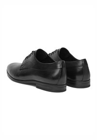 Fekete bőr dresszcipők sima textúrával, lekerekített orral és vékony fűzéses dizájnnal; alacsony, lapos gumitalppal rendelkezik.