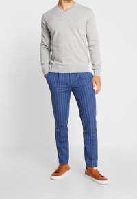 Maglione grigio a collo a V, pantaloni blu a righe e sneakers in pelle marrone. Texture a maglia liscia, vestibilità su misura ed elementi di design classici.