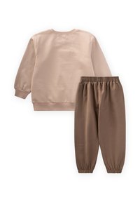 Svetlo bež pulover z okroglim ovratnikom in rebrastimi manšetami, v kombinaciji s svetlo rjavimi tapered trenirka hlačami z elastičnim pasom.