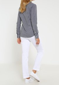 Blue and white checked shirt with long sleeves, paired with white slim-fit pants and white sneakers, showcasing a casual style.