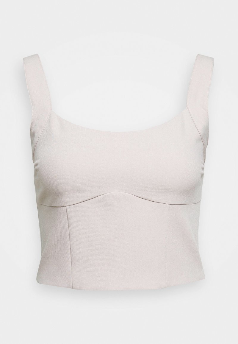 Haut court beige clair avec larges bretelles, tissu texturé et coupe ajustée. Présente une couture subtilement incurvée au niveau de la poitrine.