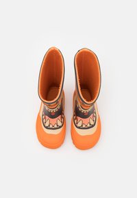 Bottes en caoutchouc imperméables orange avec un design de visage de monstre, comprenant des dents et des yeux, et une semelle texturée pour l'adhérence. L'intérieur est en tissu orange.