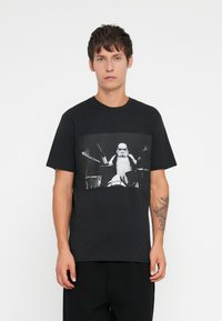 T-shirt de algodão preta com uma graphic de um Stormtrooper a tocar bateria em preto e branco. Decote redondo, mangas curtas, ajuste descontraído.