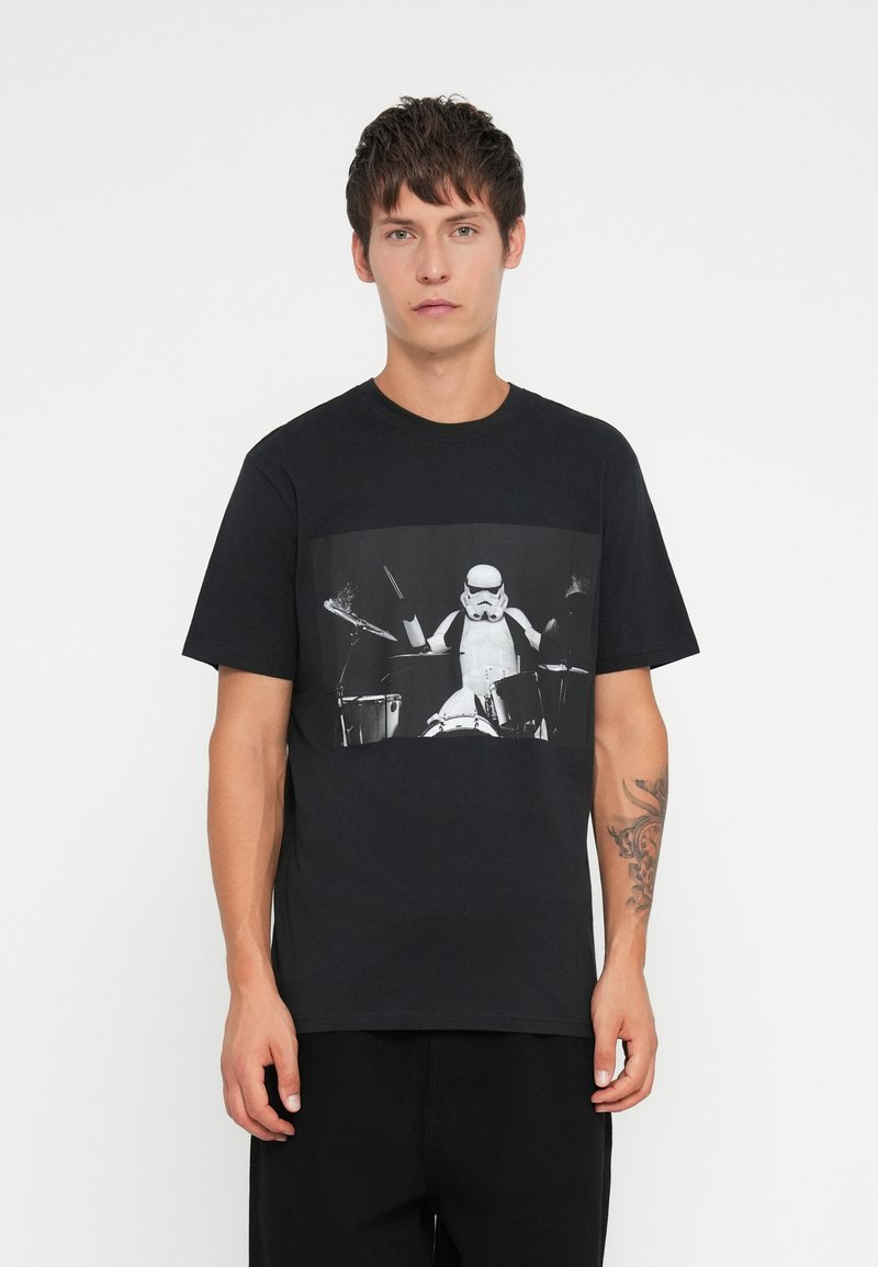 T-shirt de algodão preta com uma graphic de um Stormtrooper a tocar bateria em preto e branco. Decote redondo, mangas curtas, ajuste descontraído.