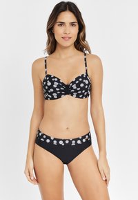 Conjunto de bikini negro que presenta un top con un diseño de lunares y una cintura a juego en la parte inferior, confeccionado en una tela suave con tirantes ajustables.