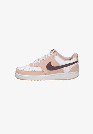 Low-top sneaker in wit en lichtroze met een donkerbruine Nike-swoosh en witte veters, platte witte zool op een witte achtergrond.