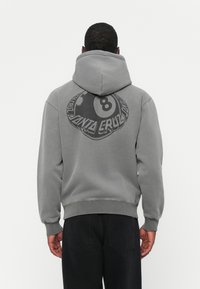 Grijze hoodie met een ronde grafische vormgeving met een "8" en de tekst "SANTA CRUZ" op de achterkant. Katoenmengsel, comfortabele pasvorm, capuchon met trekkoord.