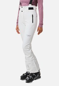 Witte skibroek met verstelbare banden, ritszakken en een logo. Zwarte skibotten met zilveren gespen. Slimfit en taps toelopend ontwerp.