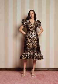 Vestido de padrão de leopardo com mangas bufantes, um decote em V e uma bainha com folhos. O material tem um acabamento lustroso. Usado com saltos beiges de tiras.