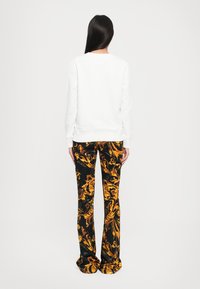 Felpa bianca con scollo rotondo, abbinata a pantaloni neri con un motivo floreale giallo. I pantaloni hanno una linea a zampa.