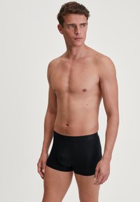 Zwarte boxershorts voor mannen van gladde stof, met een nauwsluitende pasvorm en een brede elastische tailleband met merknaam. Geen zichtbare patronen.