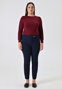 Maglione a maglia bordeaux con maniche lunghe abbinato a pantaloni slim-fit blu navy con chiusura a bottone e scarpe basse nere.