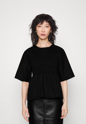 Top preto com corpete pregueado, mangas curtas e uma bainha fluida. Combinado com uma saia de couro preta com detalhes de costura.