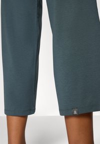 Teal bukser i cropped stil laget av myk, elastisk stoff; har en liten logo-tag på kanten, og en jevn tekstur med minimale søm detaljeringer.