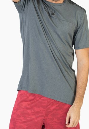 Gray athletic t-shirt with short sleeves, featuring a spider logo on the chest. Paired with bright red shorts with a camouflage pattern.