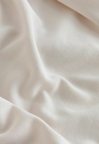 Tissu blanc texturé avec des plis doux et des ombres subtiles, mettant en valeur le motif de tissage et la surface lisse.