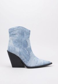 Botín de mezclilla con un lavado azul claro, punta afilada y tacón cuña negro. Presenta costuras en contraste y elementos de diseño de estilo western.