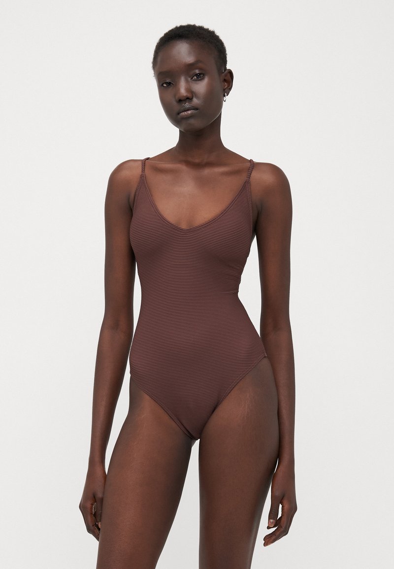 Maillot de bain une pièce marron à côtes, avec un décolleté en V et des bretelles fines et réglables, conçu pour une silhouette ajustée. Texture lisse sur toute la surface.