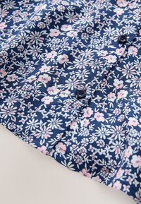 Marineblå blomsterbluse med små rosa og hvide blomster og knaplukning, lavet af letvægtsstof med en glat tekstur.