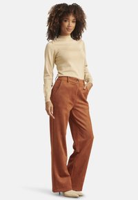 Beige long-sleeve top with shoulder button details paired with rust-colored wide-leg trousers made of a soft, textured fabric.