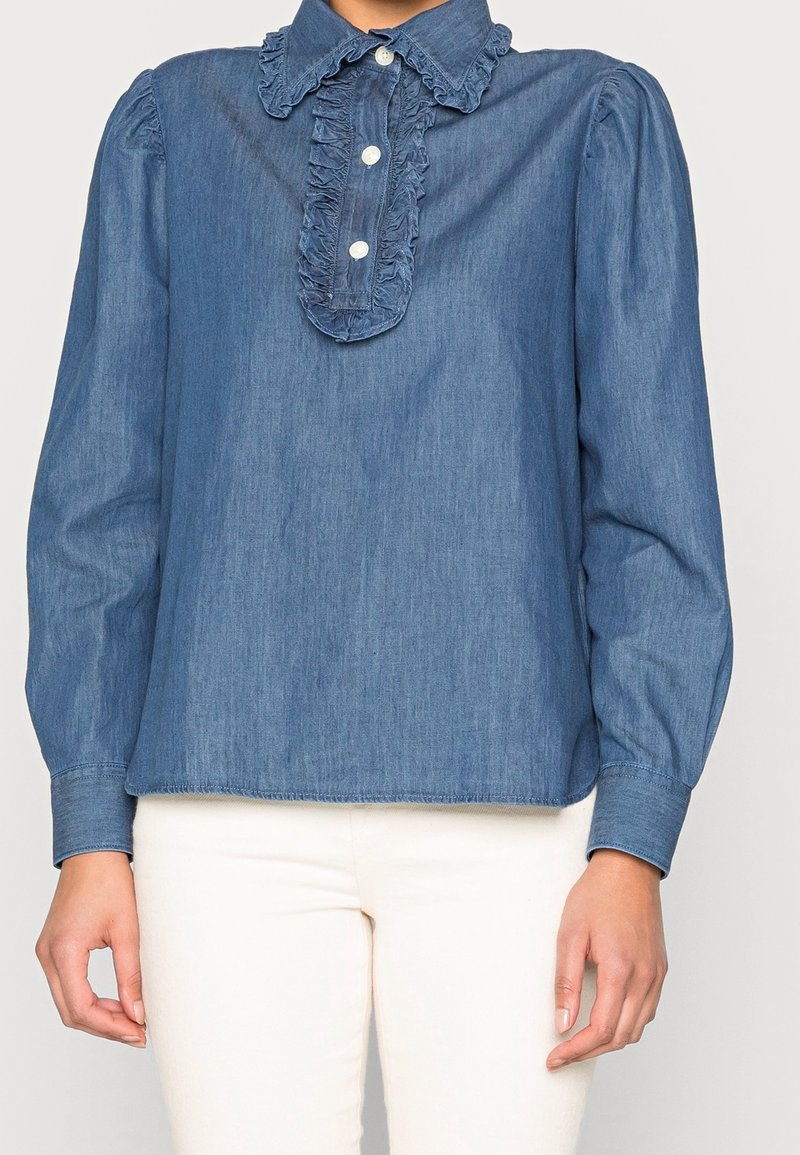 Jeansskjorta med volangkrage och knappslå, långa ärmar och en avslappnad passform. Ljusblå färg med subtil textur. Knappstängning.