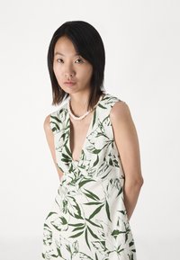 Floral-patterned dress in light cream with green leaves; sleeveless design, v-neckline, gathered detail at waist, lightweight fabric.