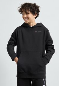Sudadera de algodón negra con bolsillo frontal, mangas largas y puños acanalados. Presenta el logotipo blanco de "Champion" en el pecho y en la manga.