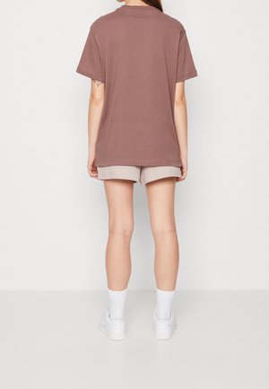 Braunes oversized T-Shirt aus Baumwolle mit Rundhalsausschnitt und kurzen Ärmeln, kombiniert mit hellbeigen, gerippten Shorts und weißen Turnschuhen.