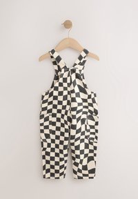 Salopette pour tout-petit à carreaux noirs et blancs avec poches avant, suspendue à un cintre en bois contre un mur uni.
