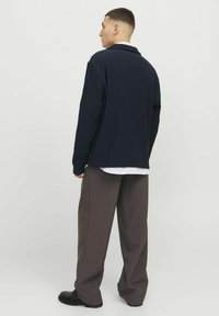 Marineblaue, gerippte Langarmbluse mit Kragen, kombiniert mit weiten braunen Hosen und schwarzen Schuhen, die eine entspannte Passform und Struktur zeigen.