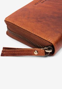 Brown leather wallet with textured finish, featuring a metal zipper closure, and a leather wrist strap with a snap button detail.
