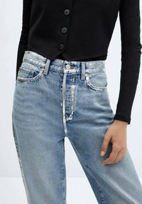 Lichtblauwe spijkerbroek met een hoge taille, wijde pijpen en distressed details. Voorzien van zilverkleurige hardware en vijf zakken. Gestyleerd met een zwarte top.