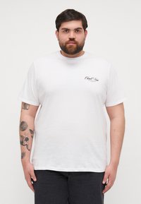 White cotton T-shirt with short sleeves; features a small black logo on the left chest area. Smooth texture, round neckline.