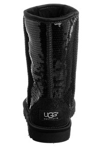 Černé kotníkové boty s flitry, s měkkým vnitřním polstrováním, logo UGG na zadní straně, plochá podrážka a texturovaný povrch.